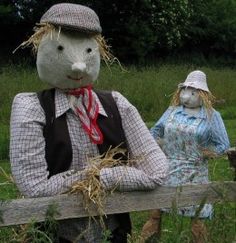 two scarecrows standing behind a wooden fence