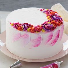 a white cake with pink icing and flowers on it sitting on a plate next to some candy