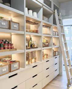 a ladder is in the middle of a room with white shelves and bins full of food