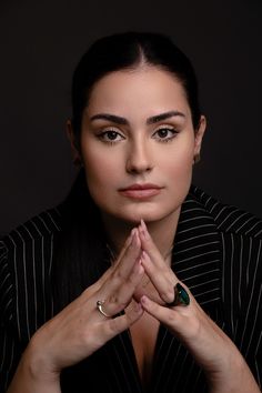 a woman with her hands folded up in front of her face, looking at the camera