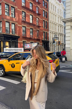 a woman with long hair walking down the street in front of a yellow taxi cab