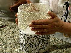 a person holding a cake in their hand on top of a counter with other people behind it