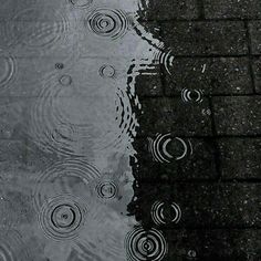 the reflection of two umbrellas and raindrops in a puddle on a sidewalk