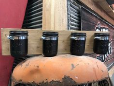 four mason jars are hanging on a wooden rack