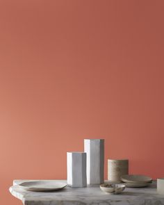 the table is set with plates, cups and vases on it in front of an orange wall