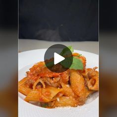 a white plate topped with pasta covered in sauce and meat next to a green leaf