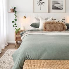 a bed with green linens and pillows in a white room next to two pictures on the wall