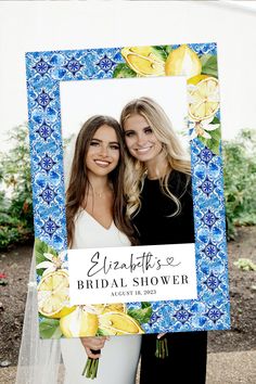 two women standing next to each other in front of a blue frame with lemons on it