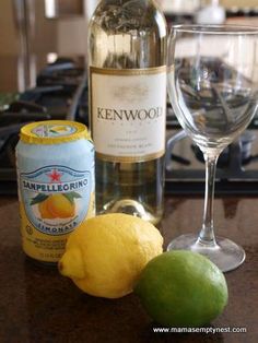 a bottle of wine and two lemons on a counter with a glass next to it