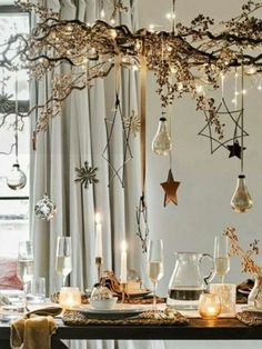 a dining room table is decorated with christmas lights and ornaments, including branches that are hanging from the ceiling