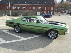 a green car parked in a parking lot next to a brick building with two windows