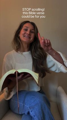 a woman sitting in a chair holding a book and pointing to the side with her finger