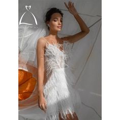 a woman in a white feathered dress posing for the camera with an umbrella behind her