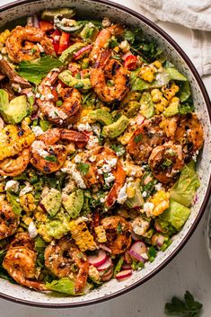 a bowl filled with shrimp, lettuce and corn salad on top of a white table