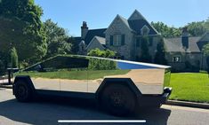 an electric car is parked on the street in front of a house with grass growing on it