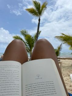 an open book sitting on top of a beach next to the ocean and palm trees