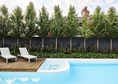 an empty swimming pool next to a wooden deck with two lawn chairs on it and trees in the background