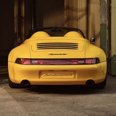 the rear end of a yellow sports car parked in front of a garage with an open door