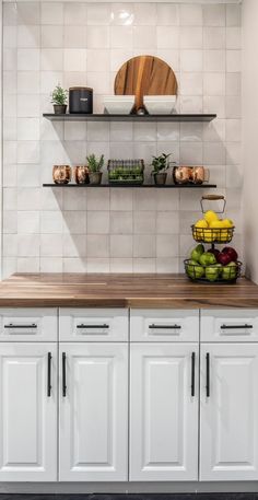 a kitchen with white cabinets and shelves filled with fruit on top of it's counter tops