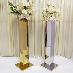 two tall vases with flowers in them sitting on top of a white tablecloth