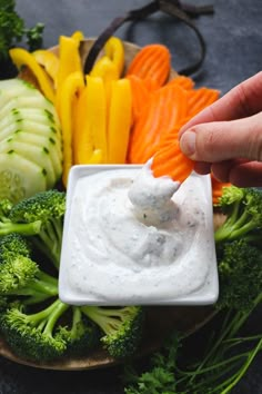 a hand dipping ranch dip into broccoli and carrots