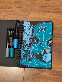 a notebook with some markers on top of it next to a pen and two pens