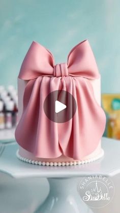 a pink bow cake on top of a white cake plate with pearls around the edges