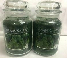 two yankee candles are sitting next to each other on a white tablecloth with pine trees in the background