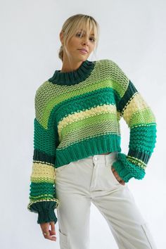 a woman standing in front of a white wall wearing a green and yellow striped sweater