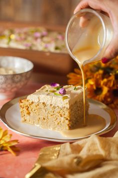 someone pouring syrup over a piece of cake on a plate with flowers in the background