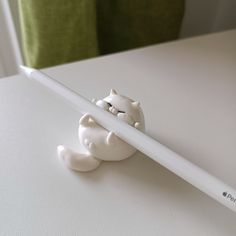 a white pencil with a cat figurine on it sitting next to a green pillow