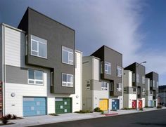 a row of multi - colored townhouses on the side of a street in front of a blue sky