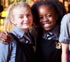 two girls in school uniforms posing for the camera with their arms around each other and smiling