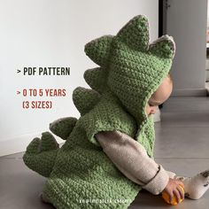 a small child in a crocheted dinosaur costume sitting on the floor with his legs crossed