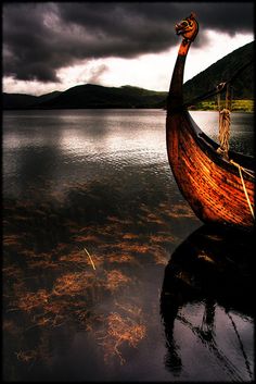 an old boat sitting on top of a body of water under a dark cloudy sky