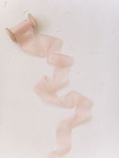 a roll of pink ribbon sitting on top of a white table next to a spool of thread