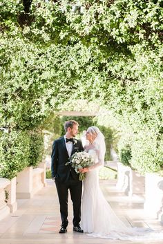 a bride and groom standing in front of an archway with greenery on either side