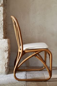 a wooden chair sitting on top of a stone floor next to a brick wall with a white cushion