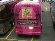 a pink bus parked in a parking lot next to other buses