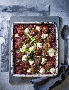 meatballs and cheese in a baking dish on a table with a spoon next to it