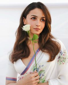 a woman holding a rose in her hand and wearing a white sari with flowers on it