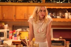 a woman standing in a kitchen next to a counter with utensils on it