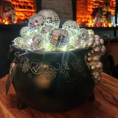 a black pot filled with lots of shiny glass balls and decorations on top of a wooden table