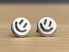 pair of silver earrings with smiley face on wooden surface in front of blurry background