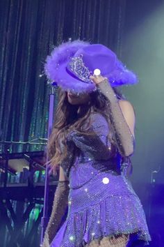 a woman in a purple dress and hat on stage