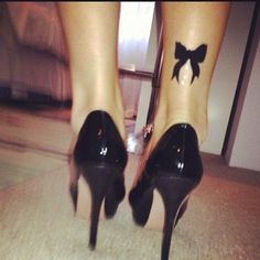 a woman's feet with a bow tattoo on her left ankle and black heels