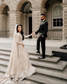 a bride and groom standing on steps in front of an ornate building holding each other's hands