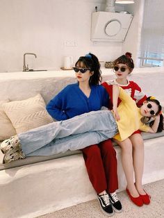 two people sitting on a couch with their legs crossed and one person wearing sunglasses is holding a doll