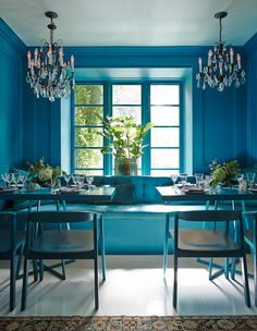 a blue dining room with chandelier and table set for four, in front of a window