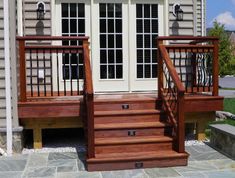 a wooden deck with steps and railings next to a home's front door